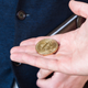 A person holds their hand out bearing a golden coin with the bitcoin symbol to another man in a blue vest.